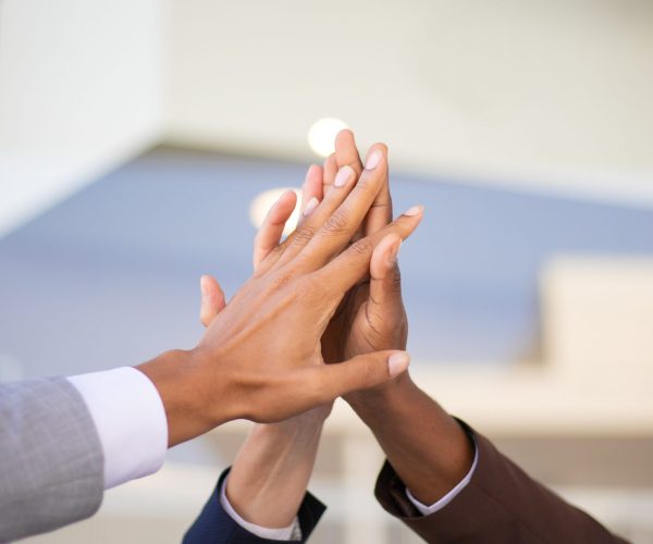 United business team celebrating success and joining hands. Group of three businesspeople giving high five to each other. Teambuilding concept